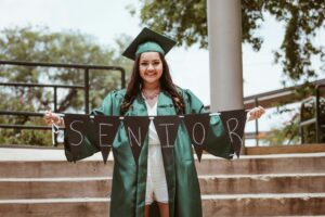 girl in cap and gown holding Senior banner